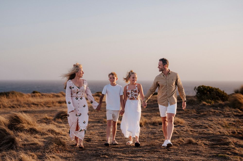 Family walks together along scenic coastal trail at sunset on grassy hilltop overlooking ocean.
