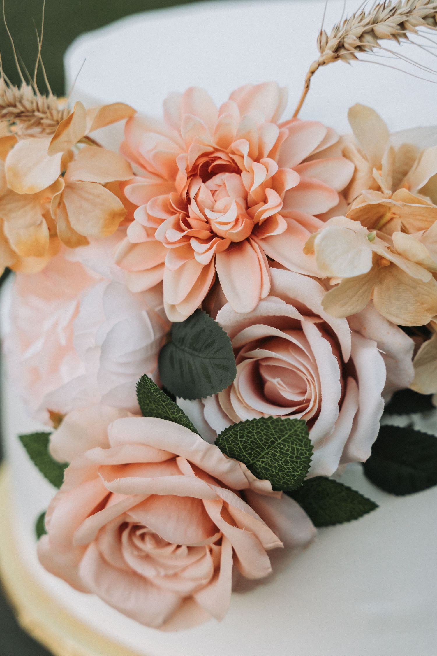 Delicate arrangement of peach roses and dahlias with wheat stems on white background.