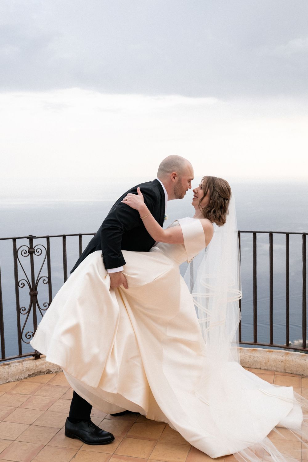 A romantic dip pose during a wedding photoshoot on a scenic coastal balcony overlooking the ocean.