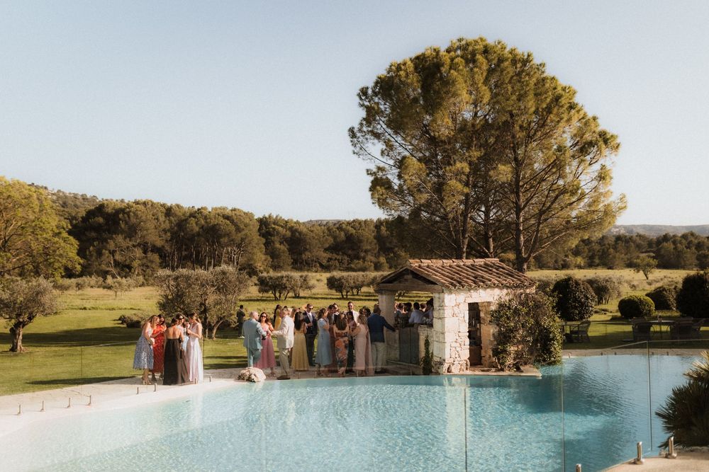 Wedding party gathers near a swimming pool with scenic landscape views.