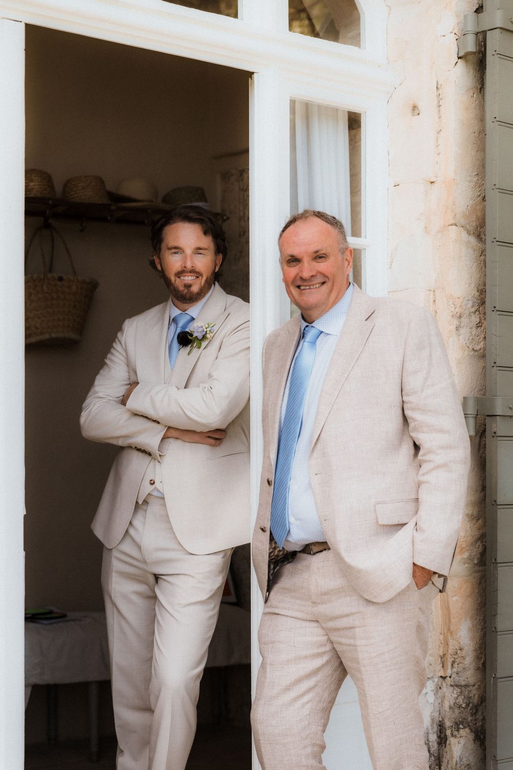 Groomsmen in cream-colored suits pose against white pillars in a playful fashion photoshoot.