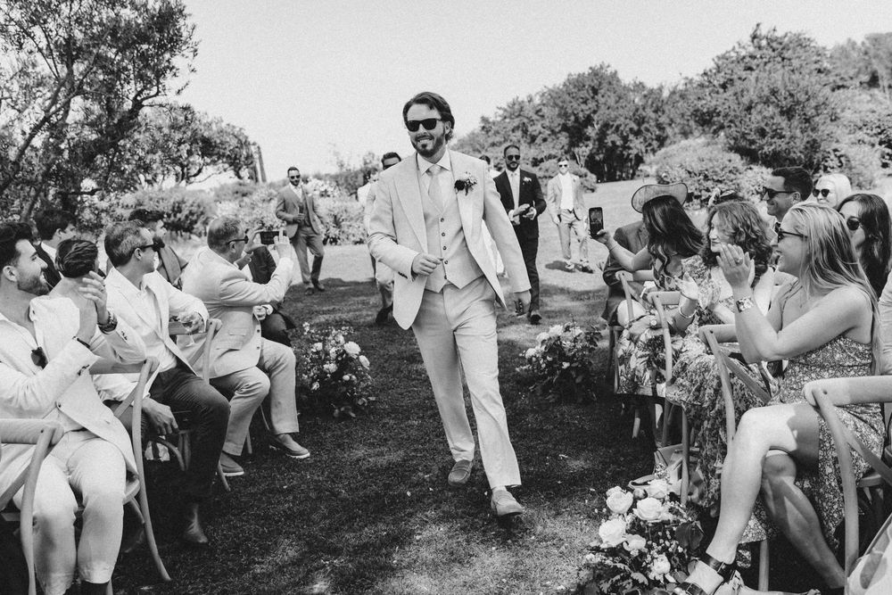Wedding party in white outfits running and playing together on a grassy hill in black and white.