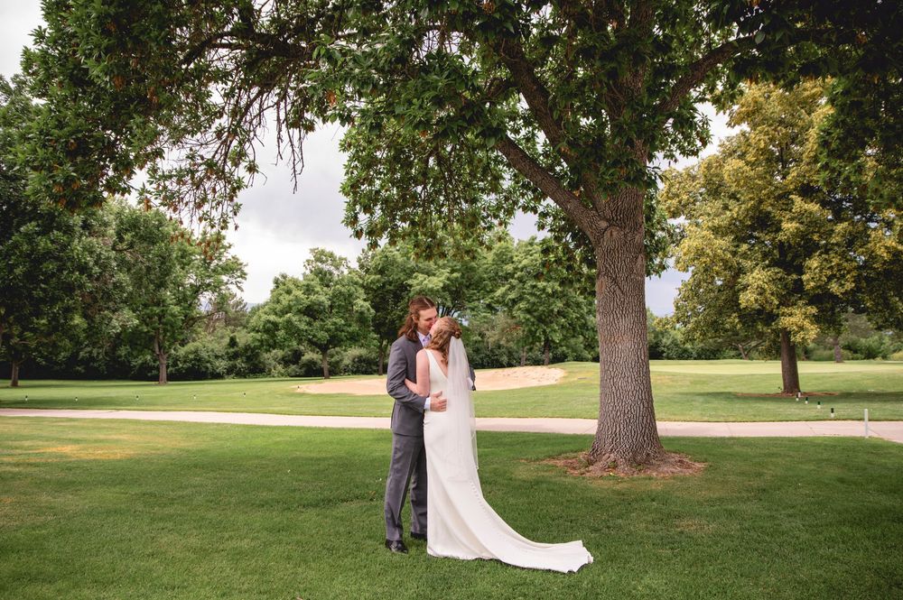 A romantic wedding photoshoot in a scenic park setting with green grass and mature trees in the background.