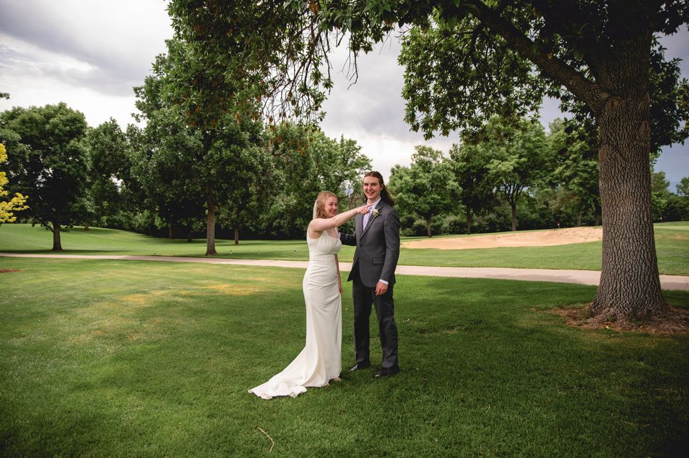 A wedding ceremony takes place under a large tree on the lush green lawn of a golf course.