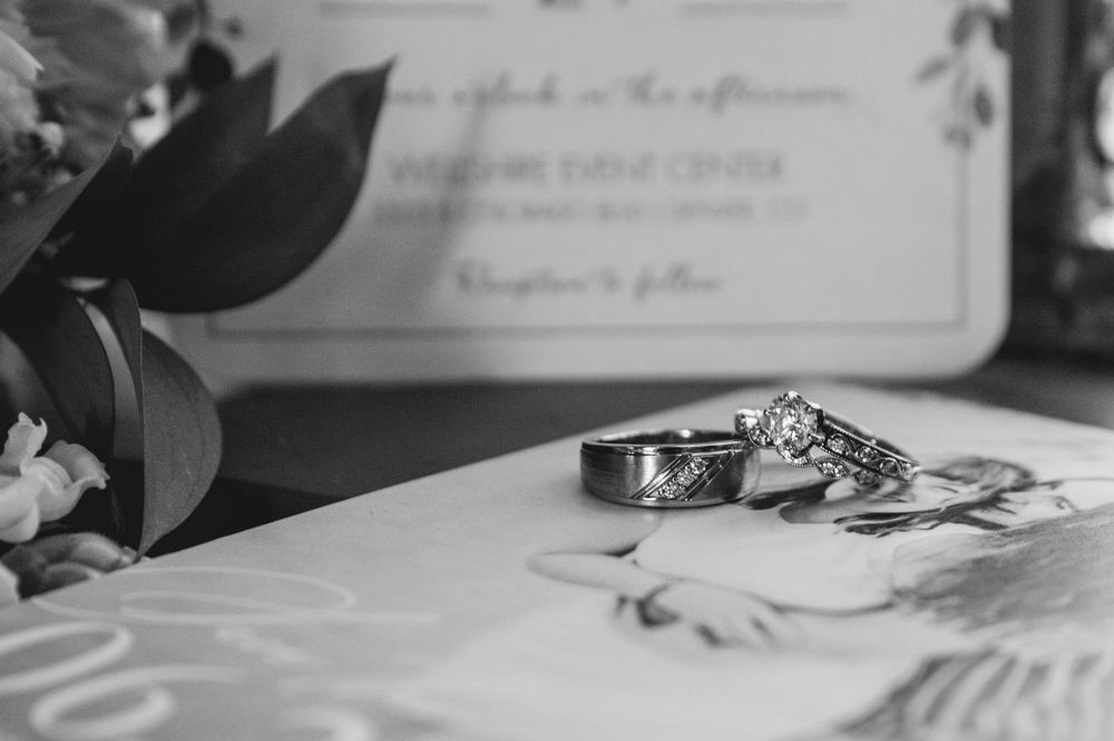 Black and white wedding rings displayed on white paper with decorative elements and greenery in the background.