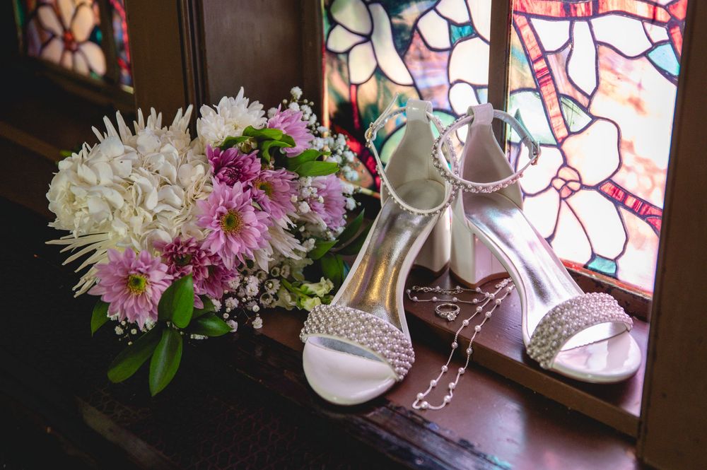 White and pink chrysanthemum flowers with wedding shoes arranged on a wooden surface in natural light.