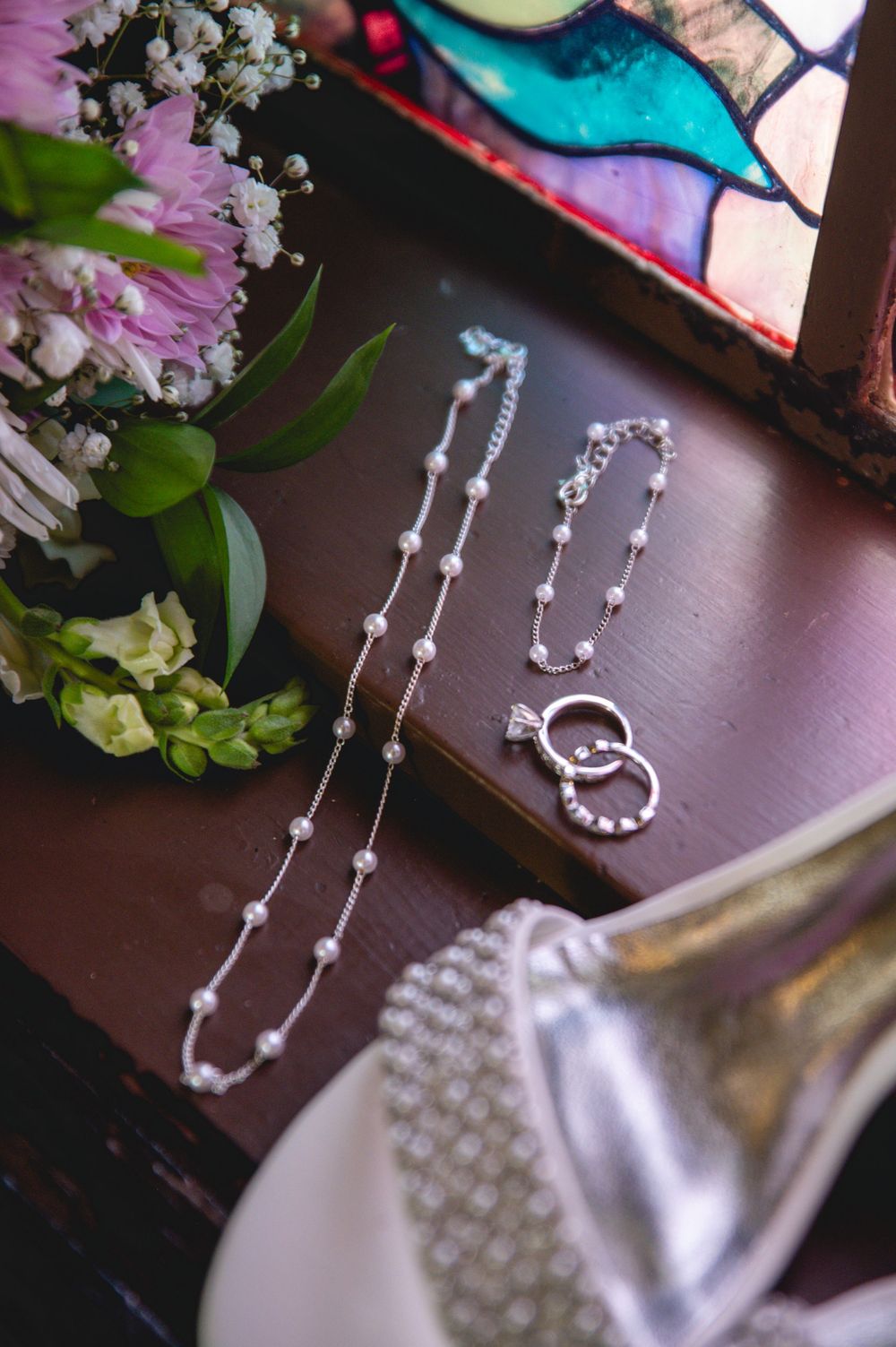 Elegant pearl necklace with silver accents displayed against a dark wooden surface with blurred floral decor.