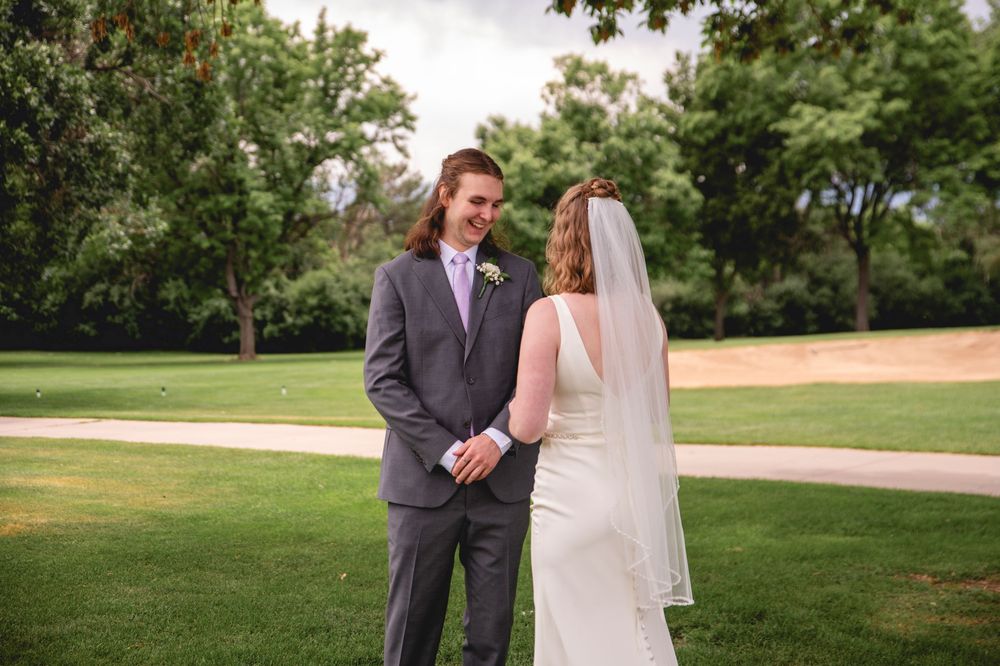 A bride and groom share an intimate moment on their wedding day while standing on lush green grass at an outdoor venue.