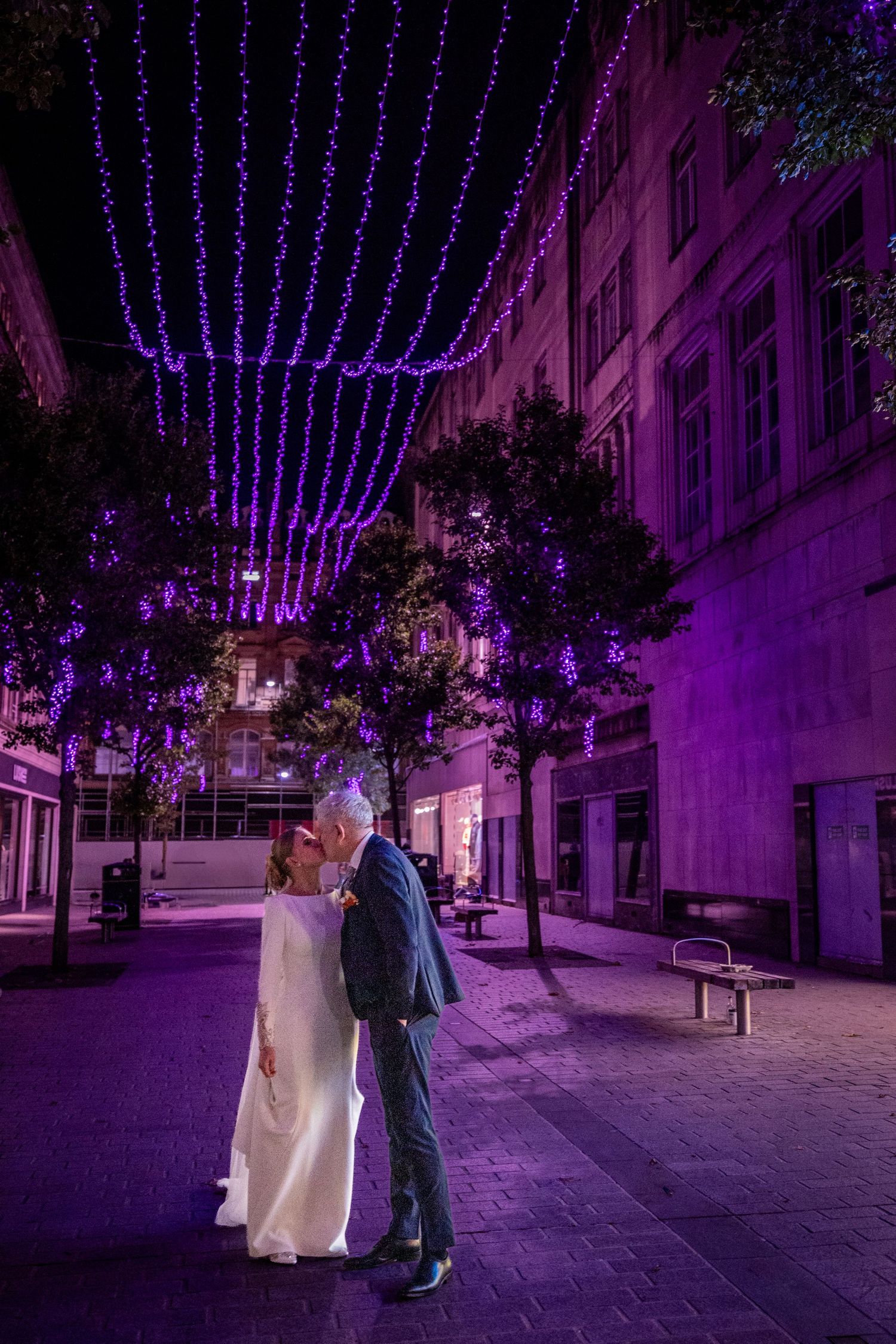 bride and groom stop to kiss in a Liverpool Street lit purple by fait lights. the Athenaeum wedding reception venue.