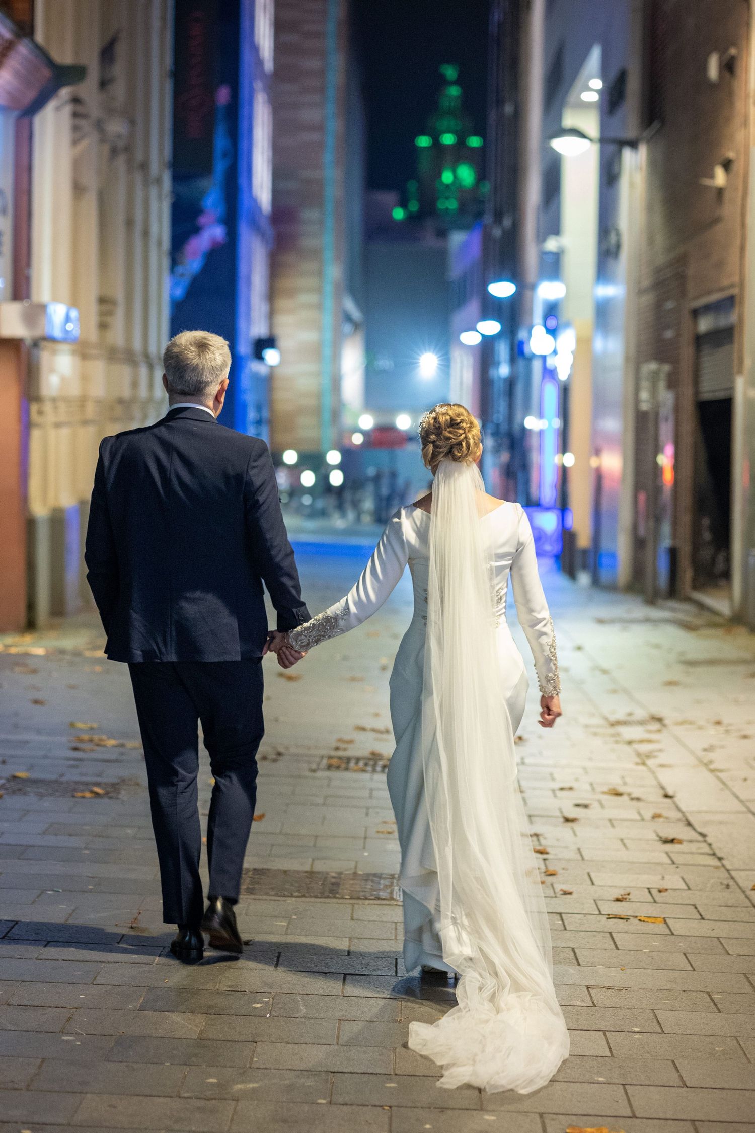 brude and groom walk away from camera in a Liverpool Street, the liver building lit up green in the distance. Stuart Morris Photography