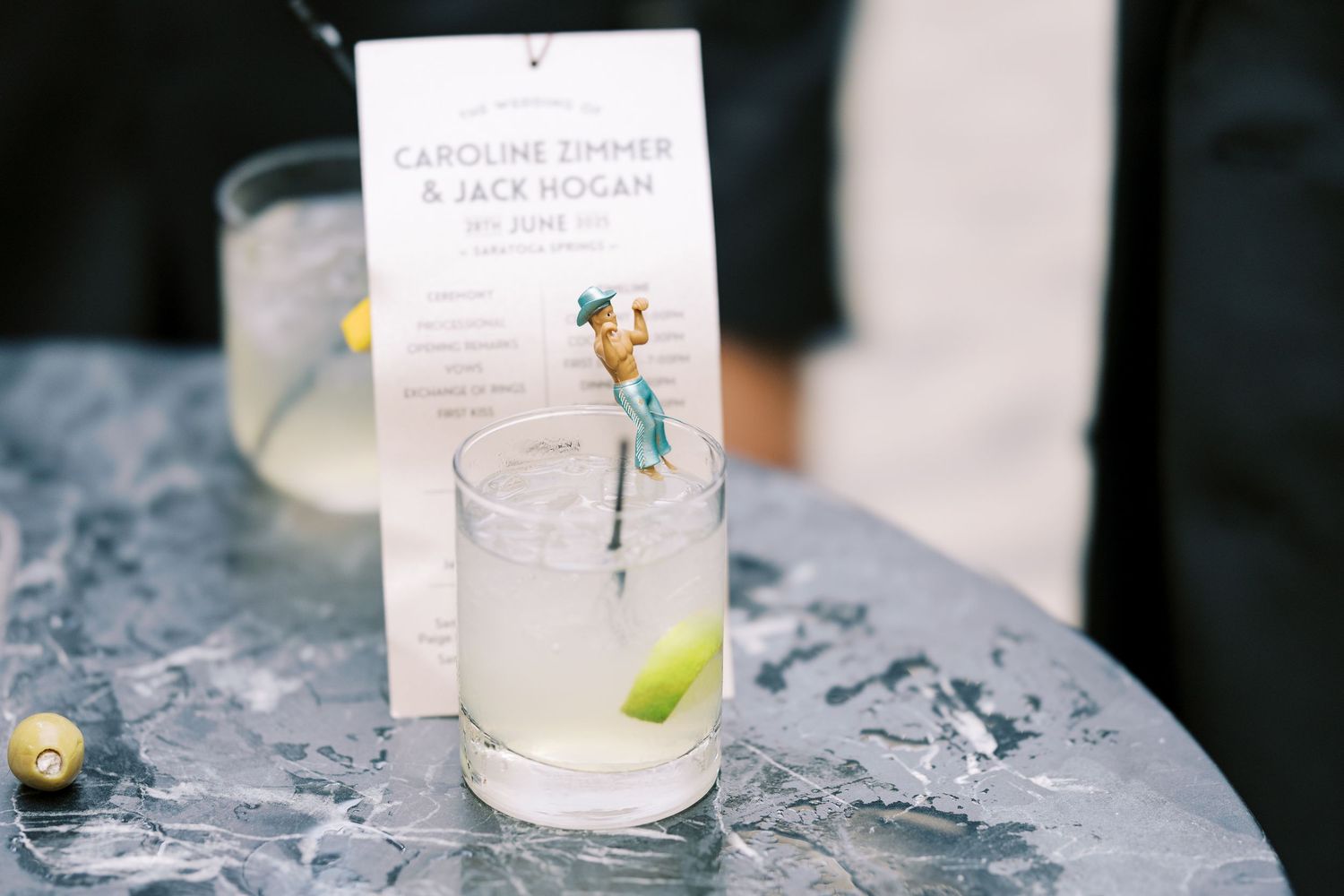 A tall cocktail glass with lime garnish and menu card sits on an ice-covered table with a decorative blue fairy accent.