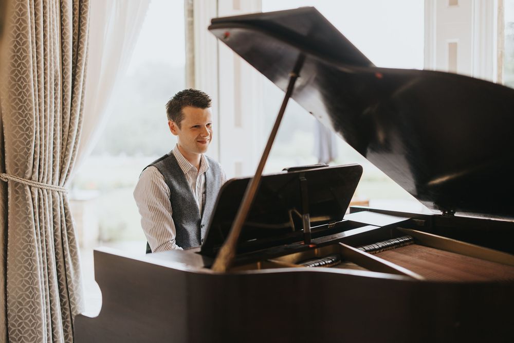 Pianist in elegant grey suit plays grand piano by window in bright sunlight at Cave Castle - taken by Grimsby photographer.