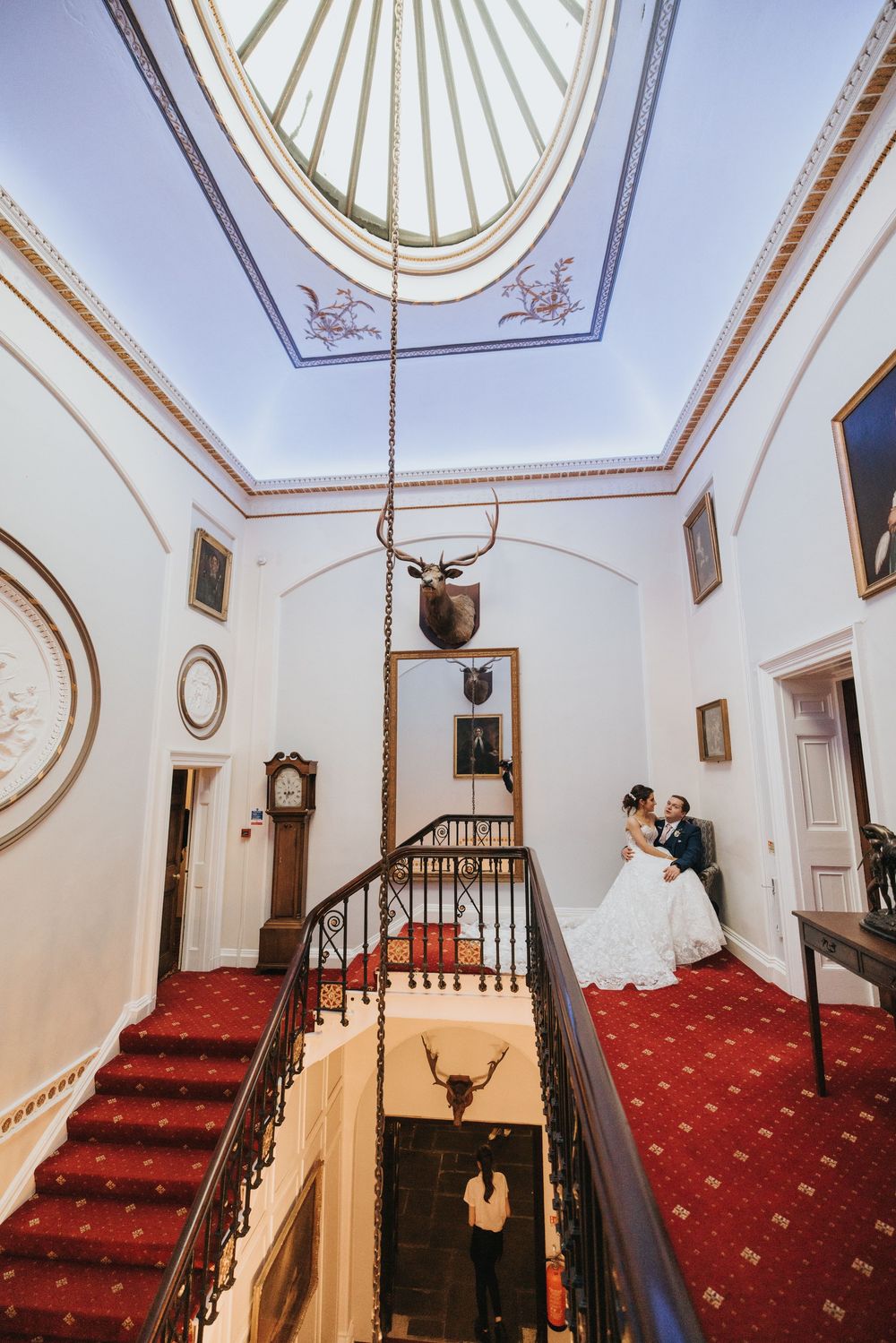Spiral staircase in a Victorian-style building with red carpet and white walls featuring elegant skylights and wall sconces at Cave Castle.