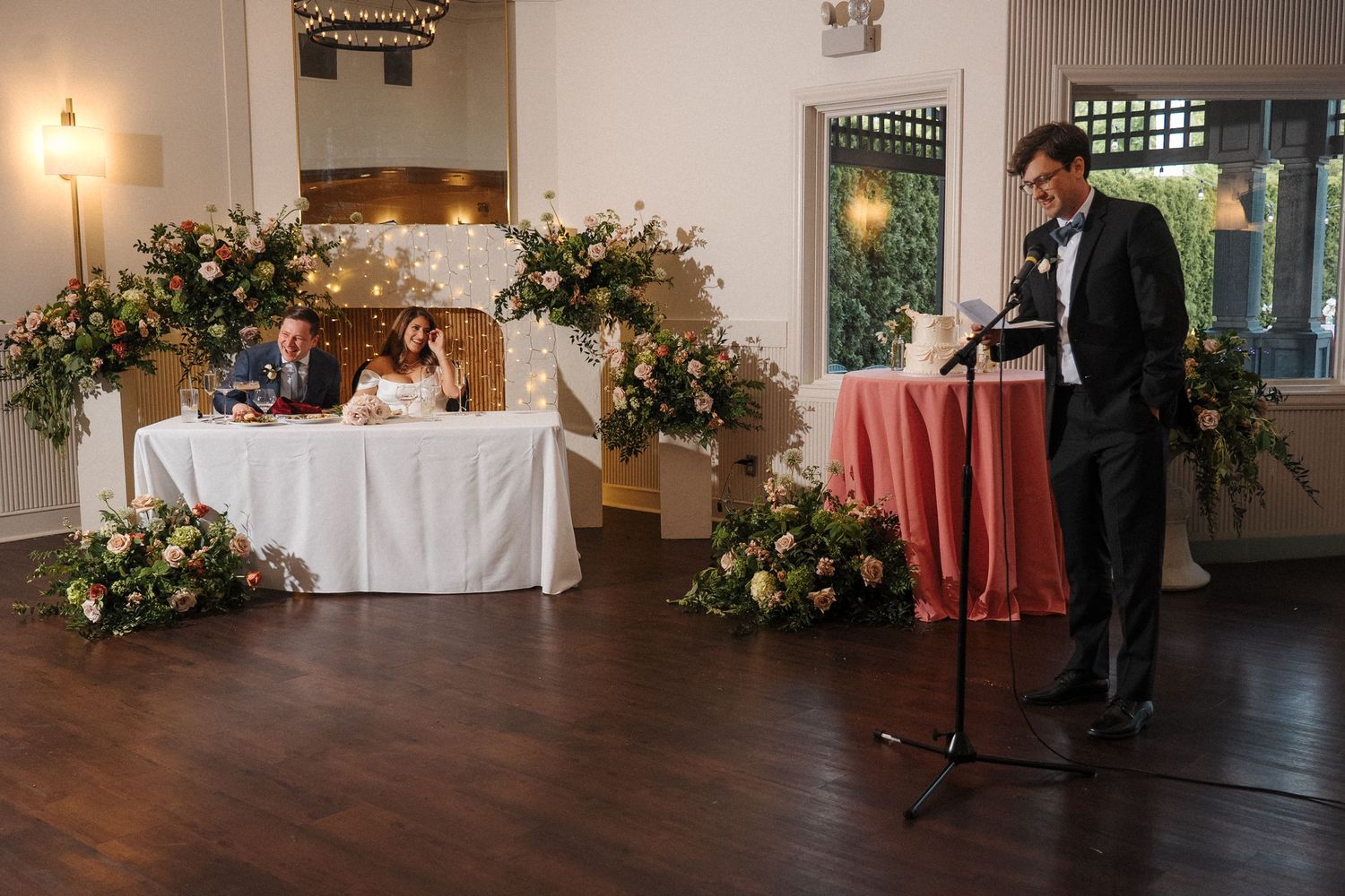 An elegant wedding reception venue with twinkle lights, floral arrangements and white tablecloths.