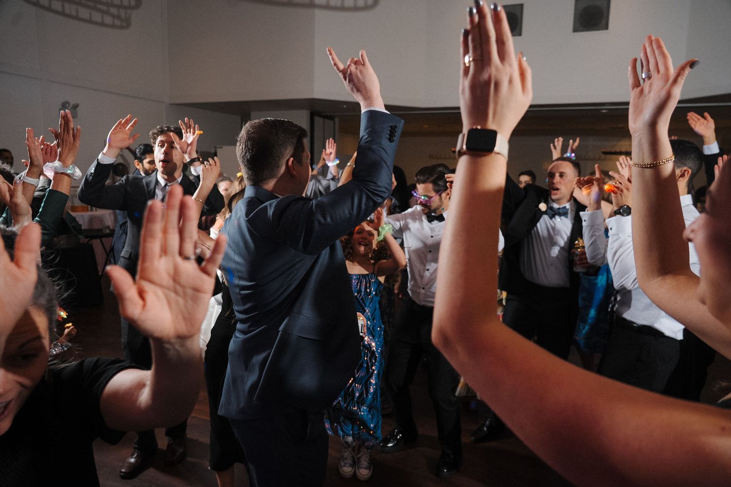 Crowd with raised hands dancing and celebrating together at a lively indoor wedding reception party.