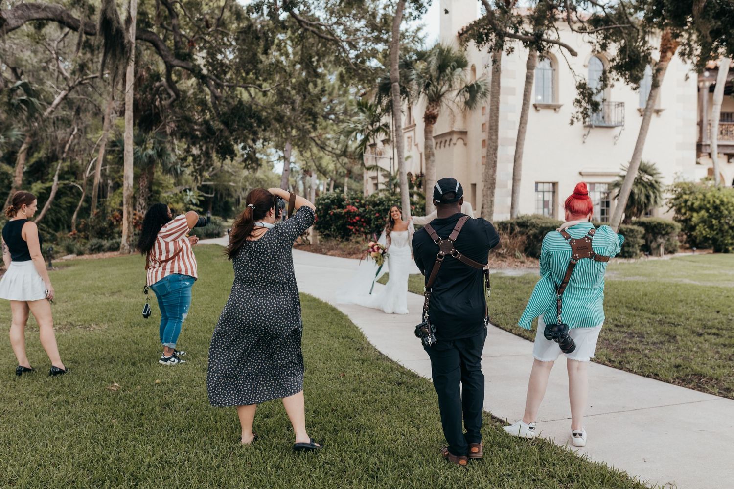 Wedding party members walk together on a paved garden path during a casual outdoor celebration.