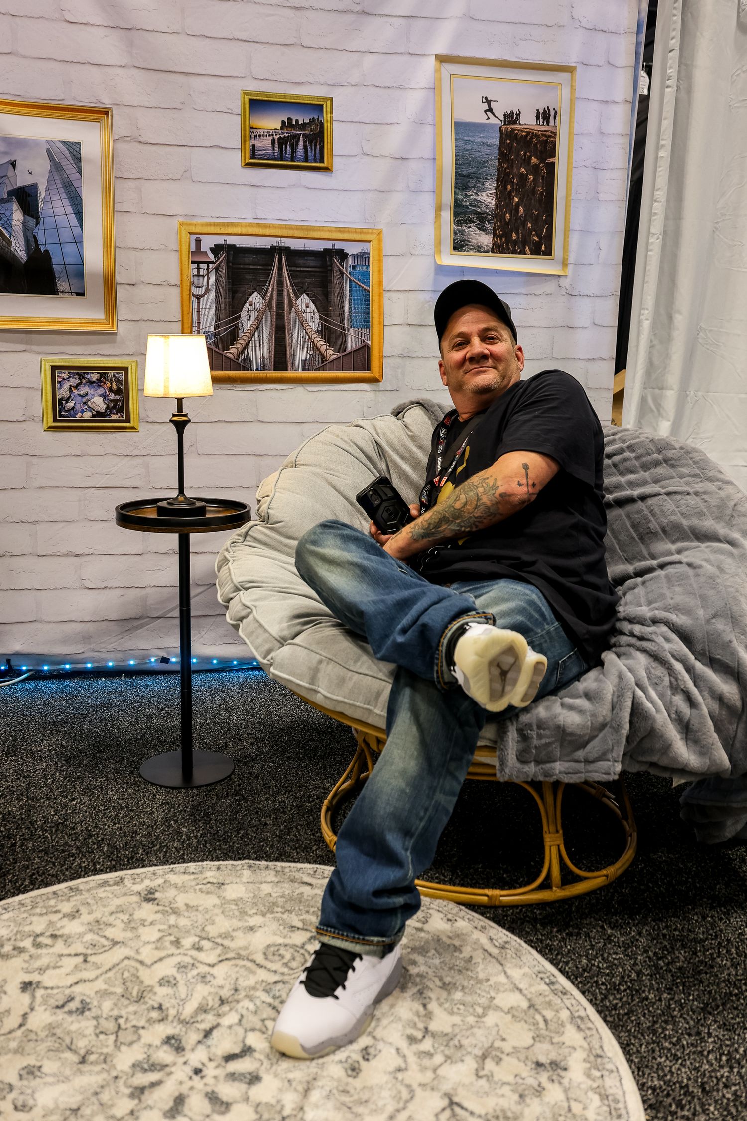A person rests on a curved rocking chair with dark cushions against a white wall decorated with framed artwork.
