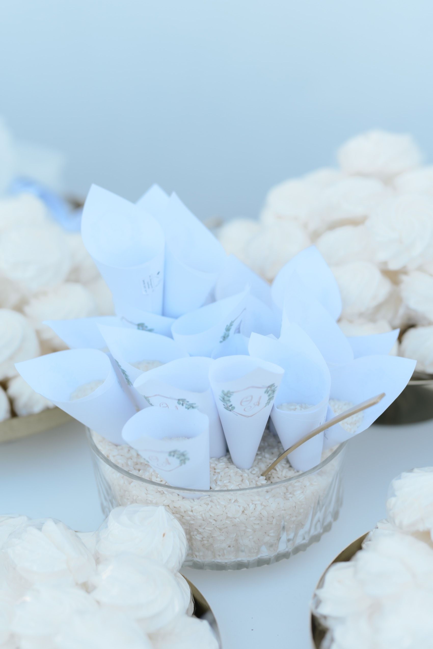 White paper cones filled with rice or confetti arranged in a vintage glass bowl against a light blue background.