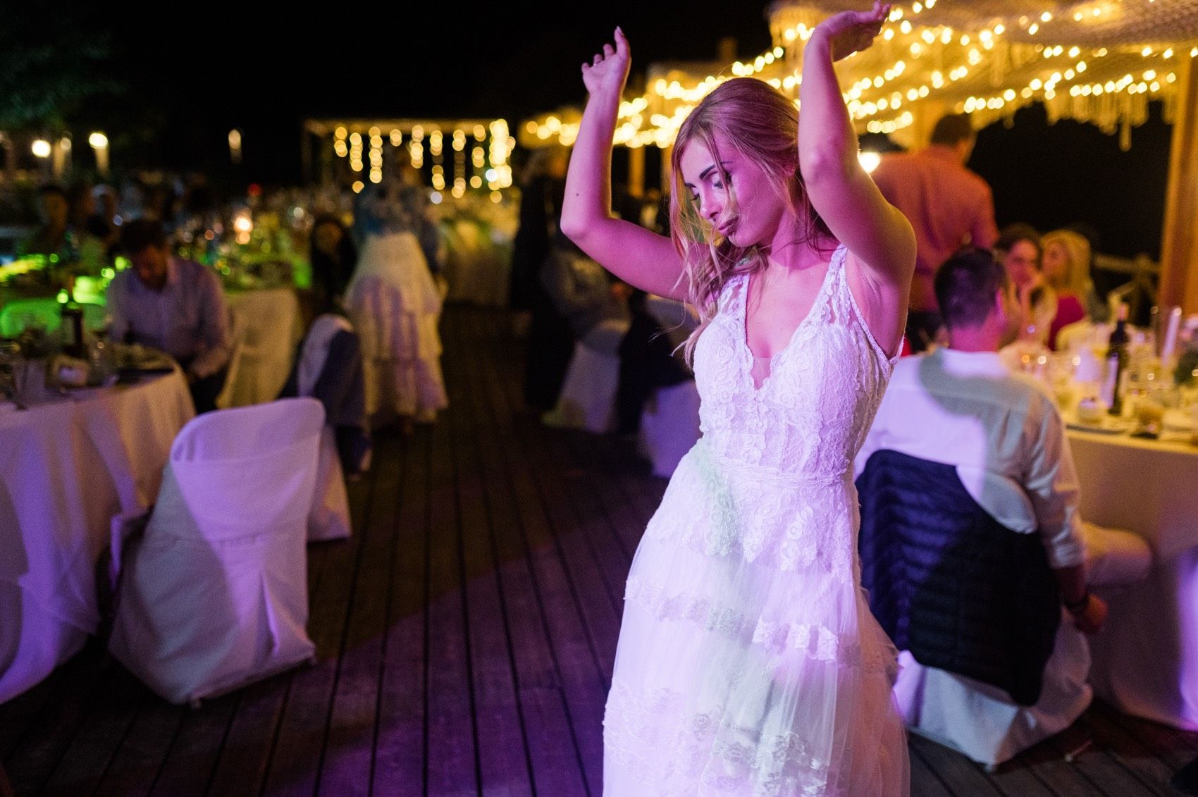Wedding guests dance and celebrate on a colorfully lit dance floor during an evening reception.