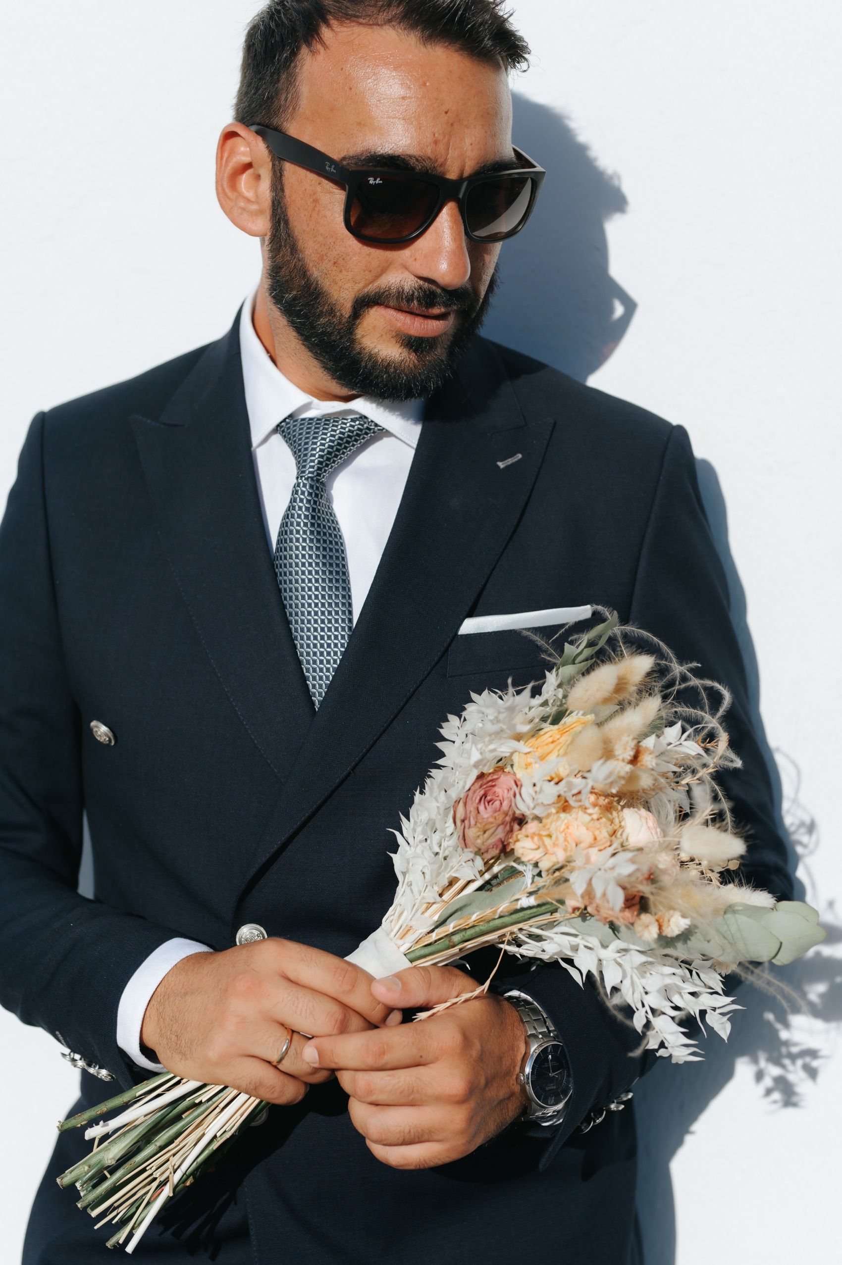 A person in a dark suit and sunglasses examines a delicate white floral bouquet in a series of progressive shots.