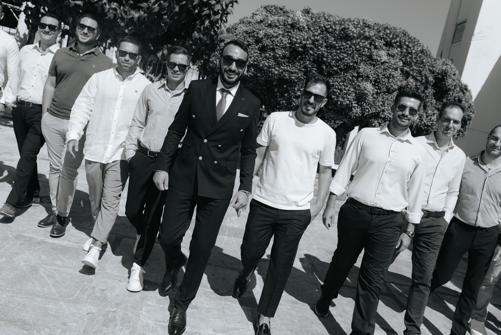 A black and white vintage photograph shows a group of people walking together in a row outdoors, with one wearing a suit.
