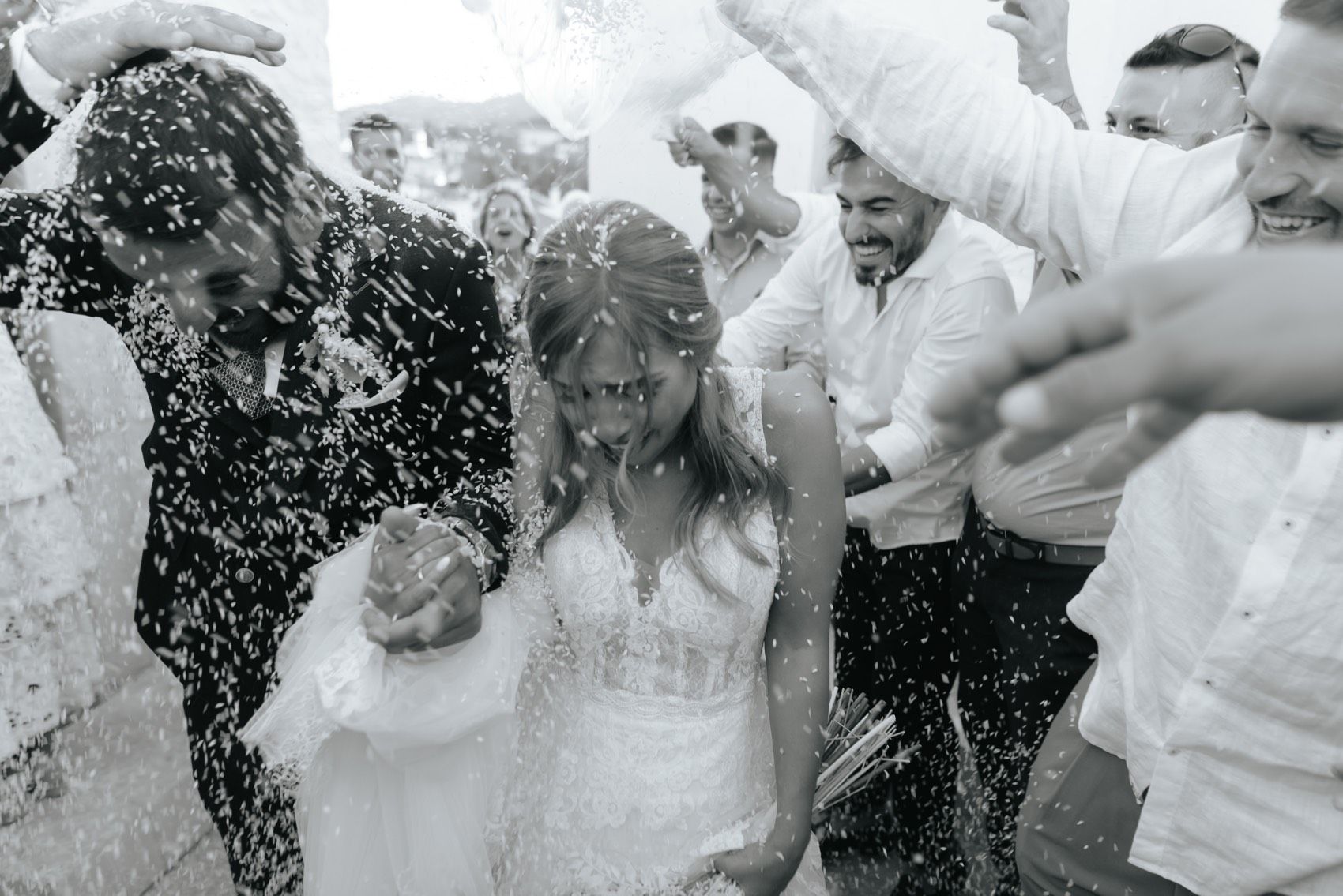 Wedding guests throw confetti and celebrate around a happy couple during outdoor reception festivities.