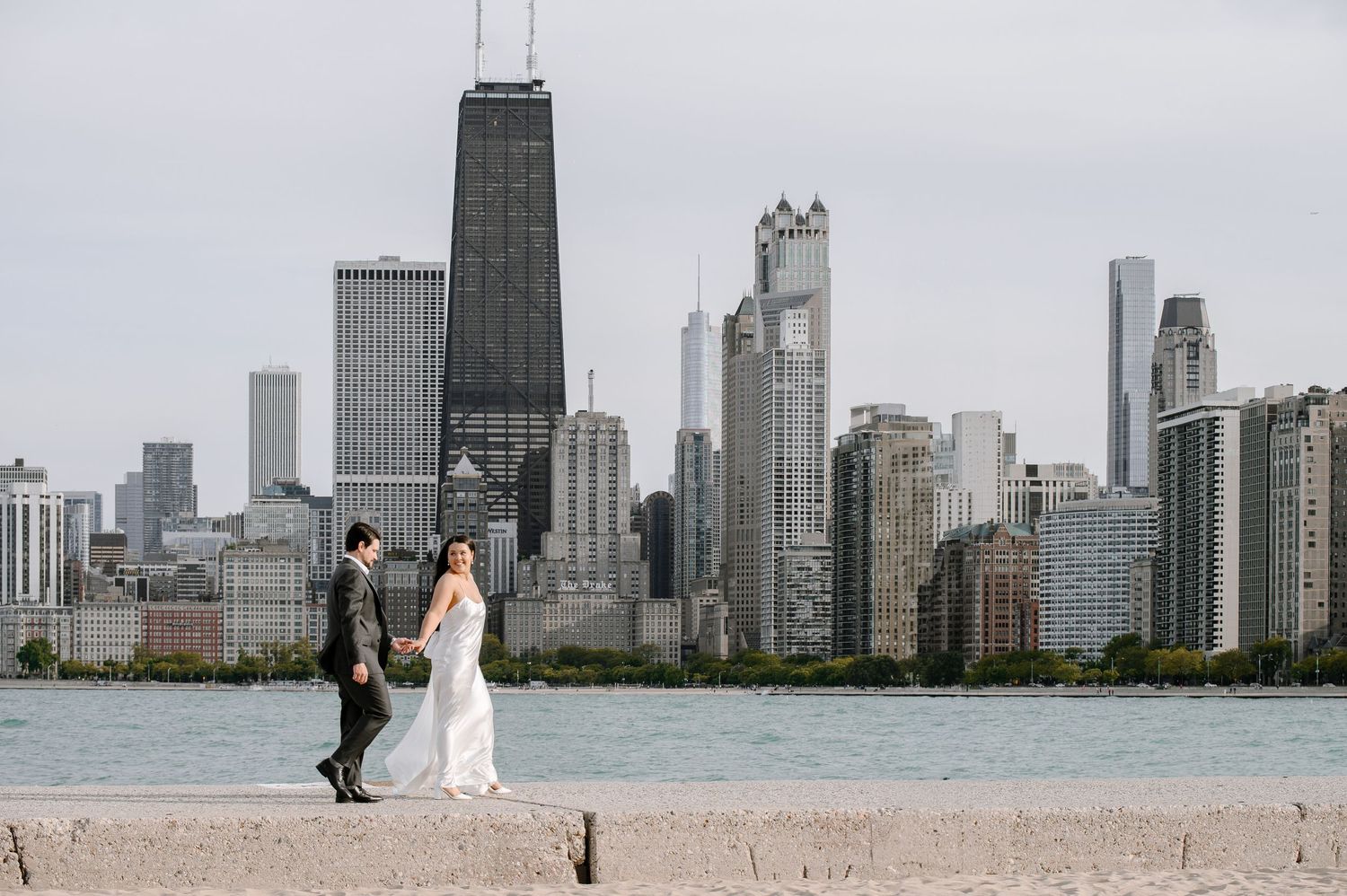 A couple poses on the shore of Lake Michigan with the iconic Chicago skyline featuring the John Hancock building in the background.