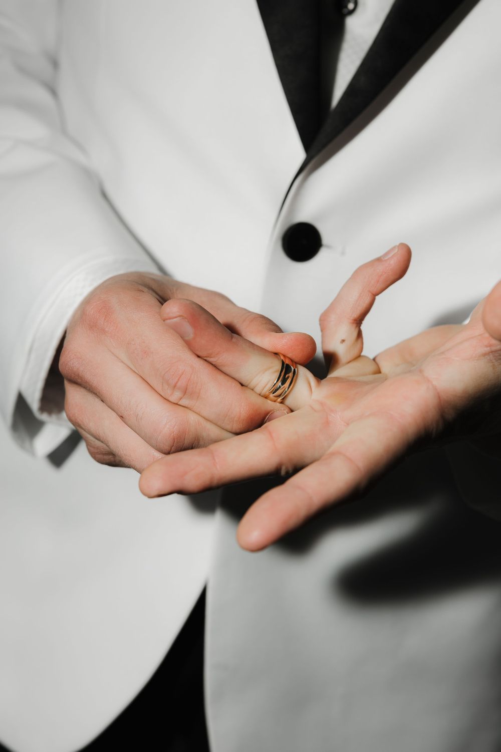 Close-up of hands holding wedding ring against white tuxedo jacket.