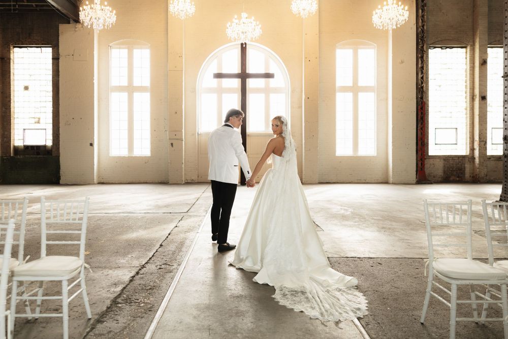 Wedding ceremony in an elegant church venue with arched windows, crystal chandeliers and white chairs.