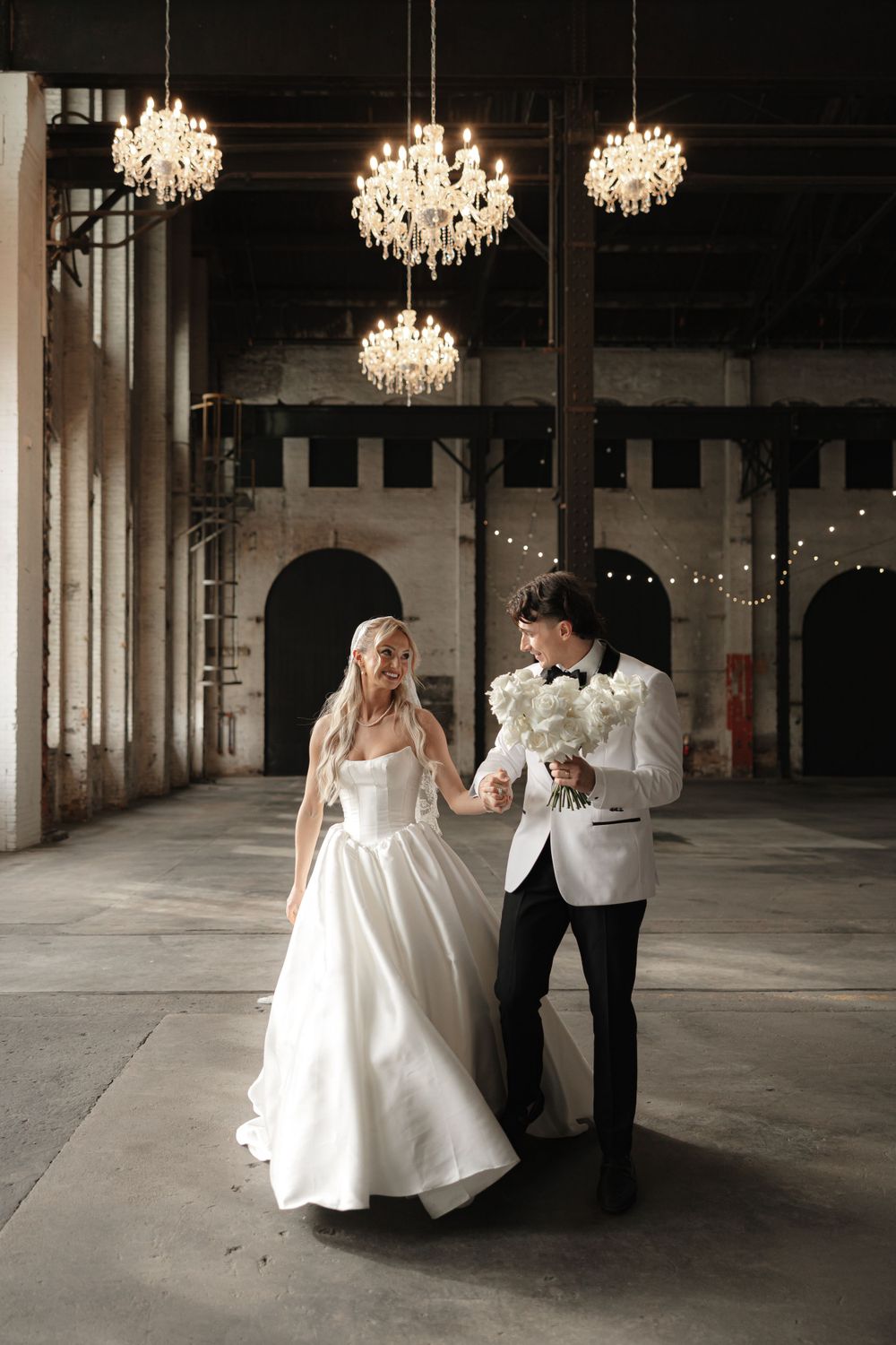 Elegant couple dancing beneath crystal chandeliers in a grand ballroom setting.