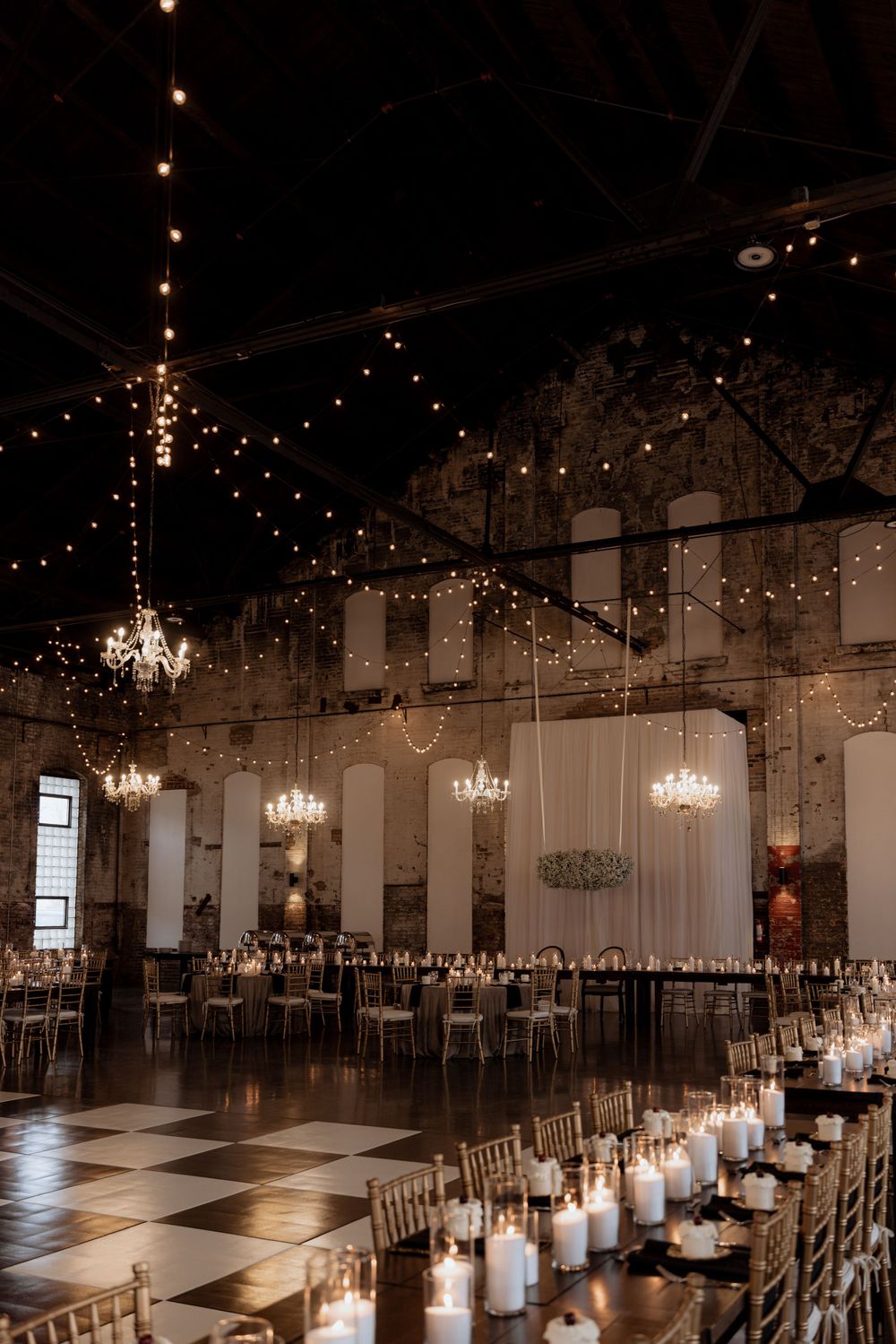 Reception hall with elegant chandeliers and string lights creating a romantic ambiance.