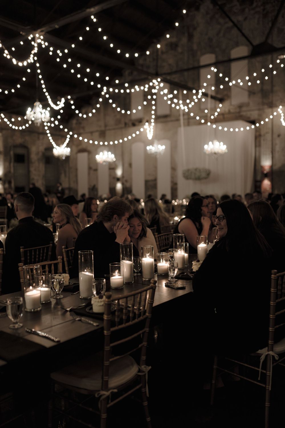Candlelit wedding reception with string lights and chandeliers creating an intimate atmosphere.