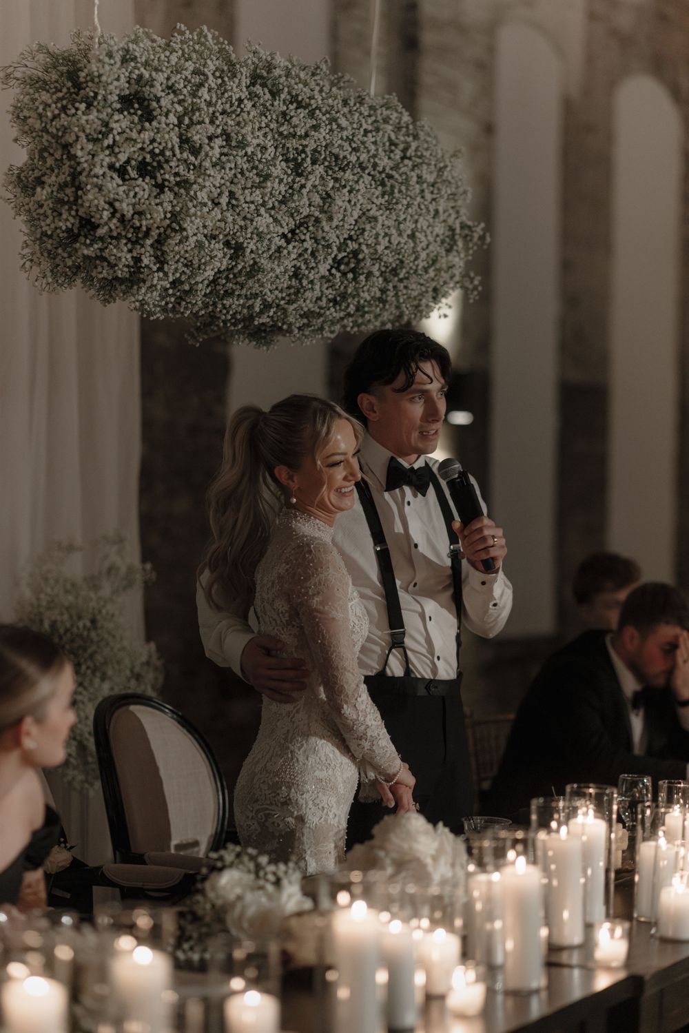 Wedding reception moment under baby's breath cloud installation with candlelit table setting.