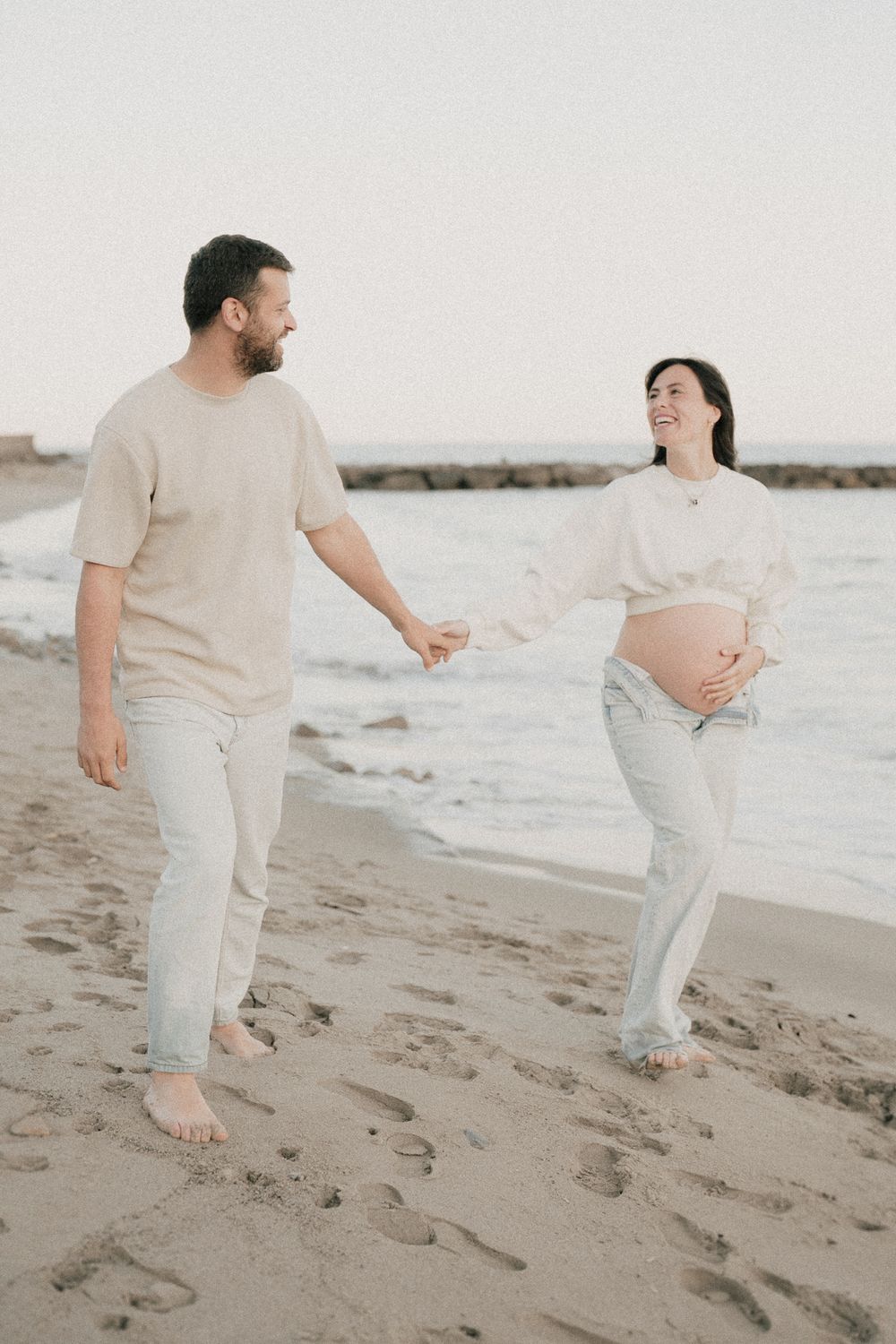 una fotografia maternity con mamma e papà che camminano sulla spiaggia in liguria