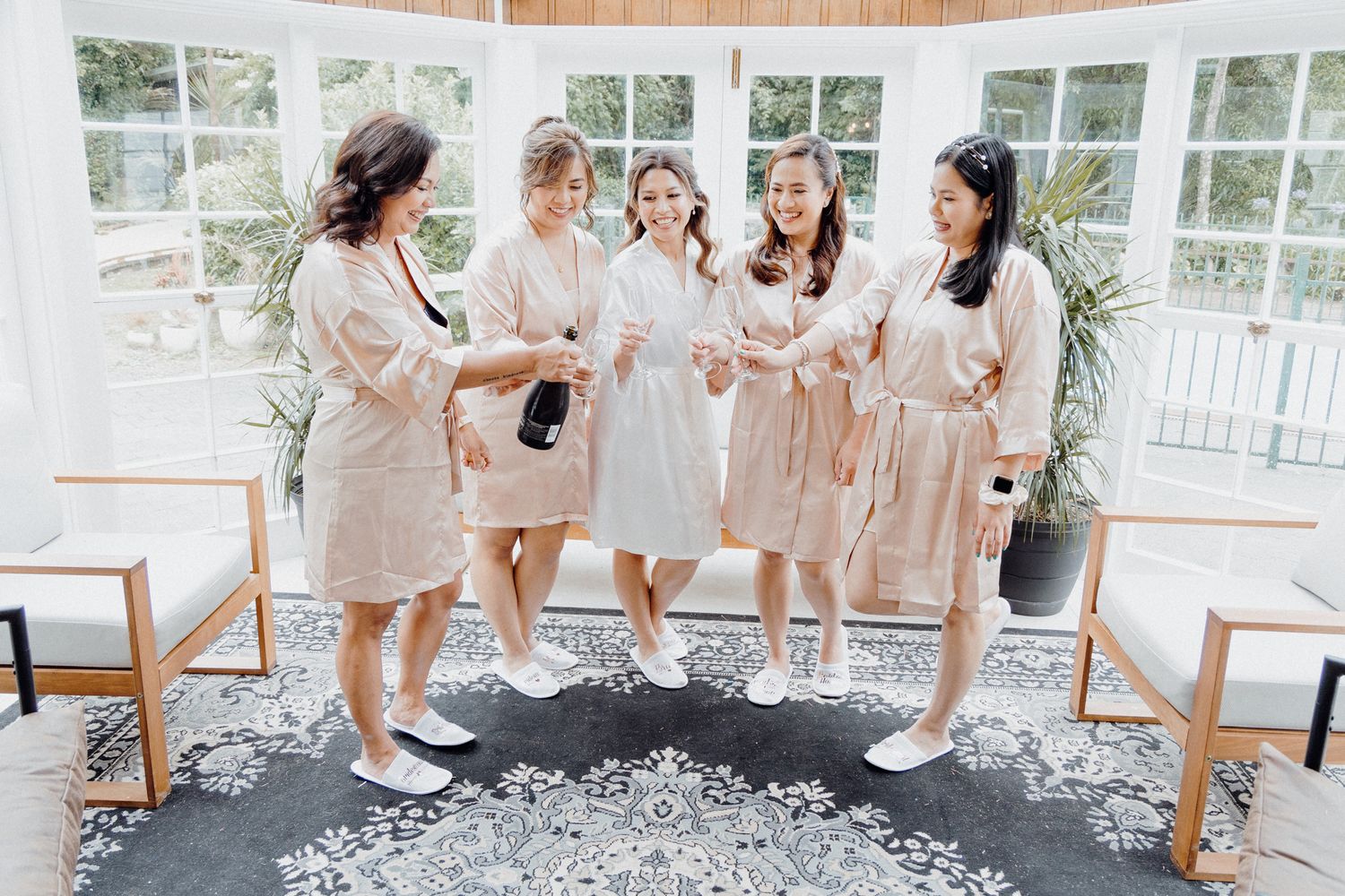 Five people wearing matching beige robes stand together captured by Apertured Media Auckland Wedding Photographer.