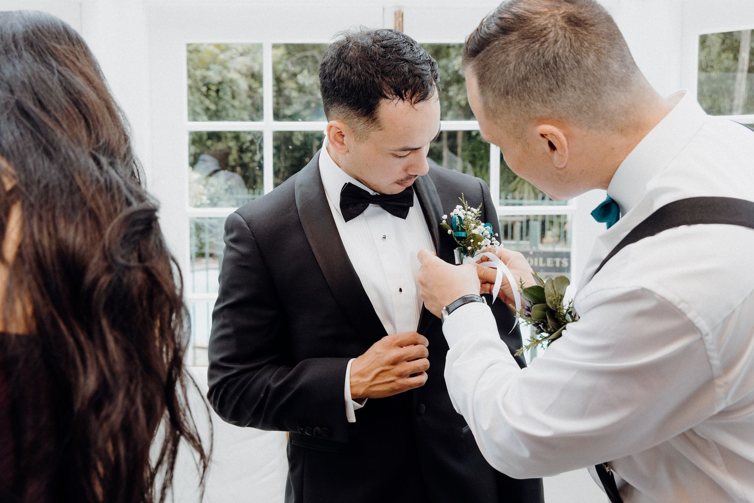 Two people in formal attire adjusting a boutonniere before an event captured by Apertured Media Auckland Wedding Photographer.