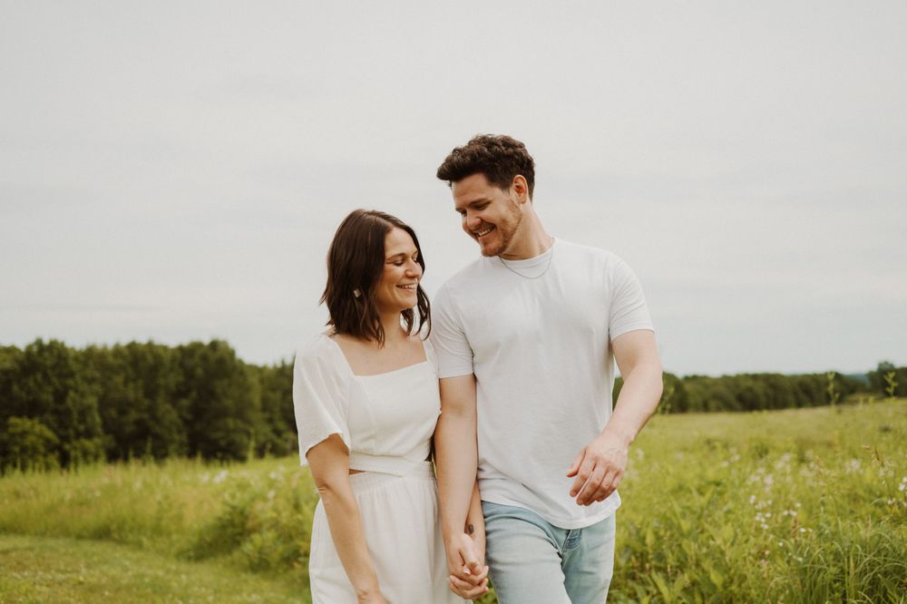 A couple share a joyful moment while walking together in a green summer field.