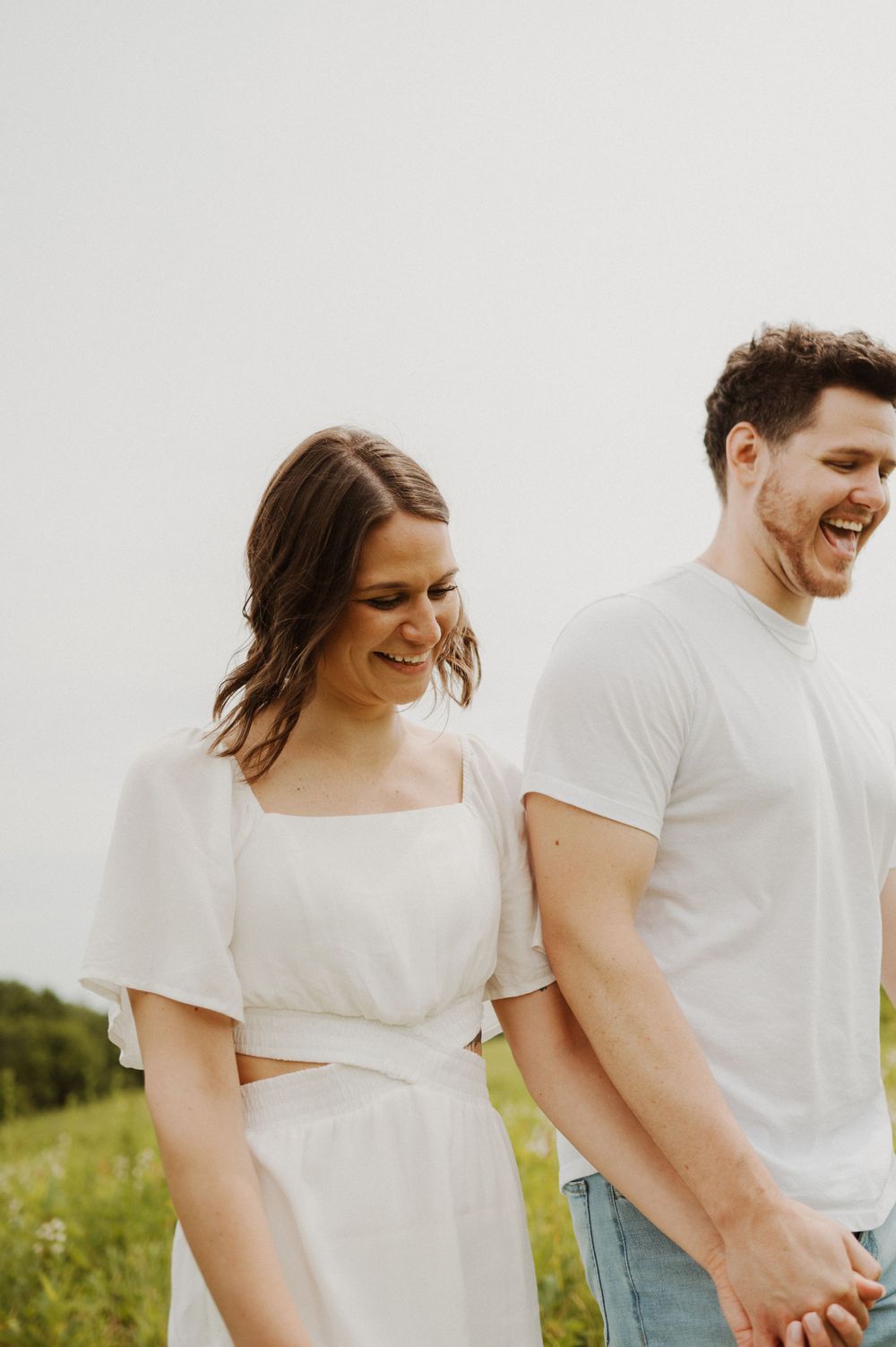 A couple share genuine laughter together in a sunlit meadow.