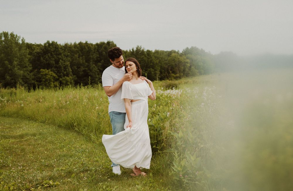 A couple embrace in a dreamy summer meadow with soft focus edges.