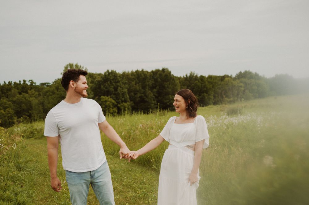 A couple hold hands while walking through a misty summer field.