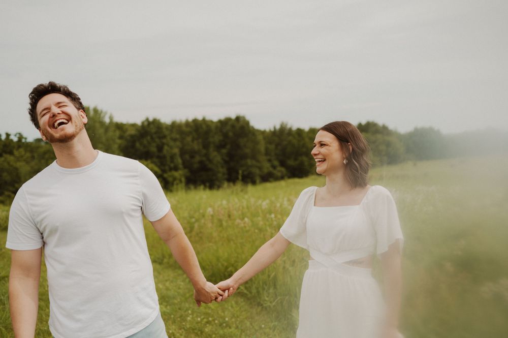 Couple embracing and laughing joyfully in a sunny meadow with wildflowers.