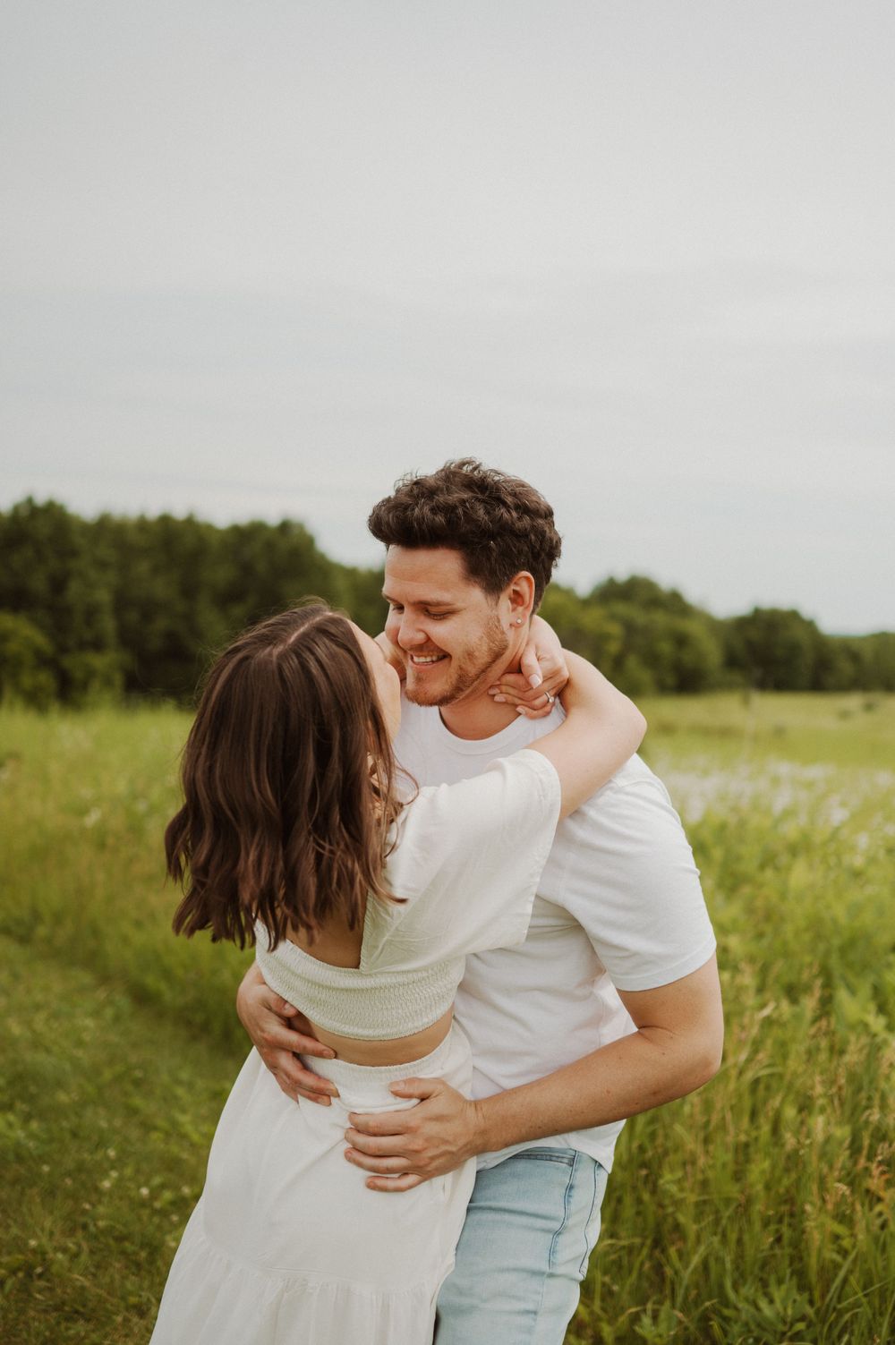 Romantic couple in white outfits dancing in a green summer field.