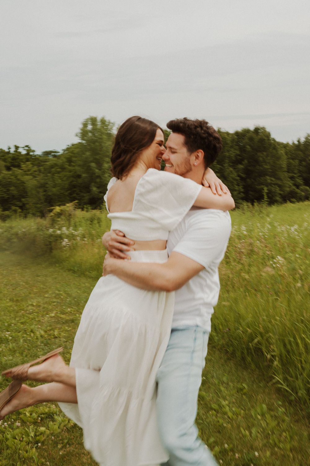 Playful couple in white clothes dancing and embracing in a grassy field.