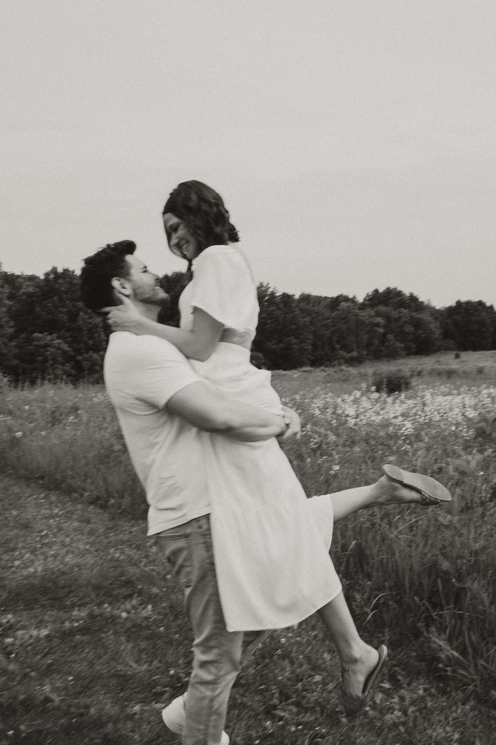A romantic black and white photo of a couple in a field, with one person lifting the other in an embrace.