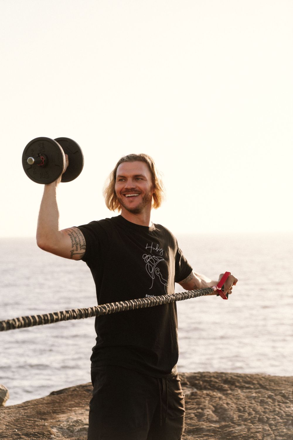 Health Coach exercises outdoors at sunset holding a dumbbell and rope near the ocean during a personal branding shoot in Sydney.