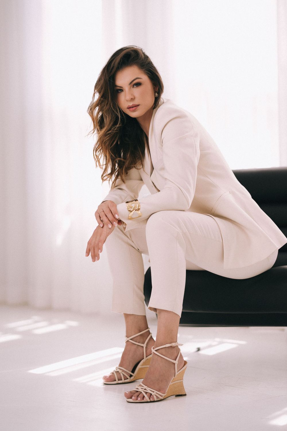 Branding Photography Sydney captures an entrepreneur in a white pantsuit posing elegantly on a dark couch, showcasing storytelling.