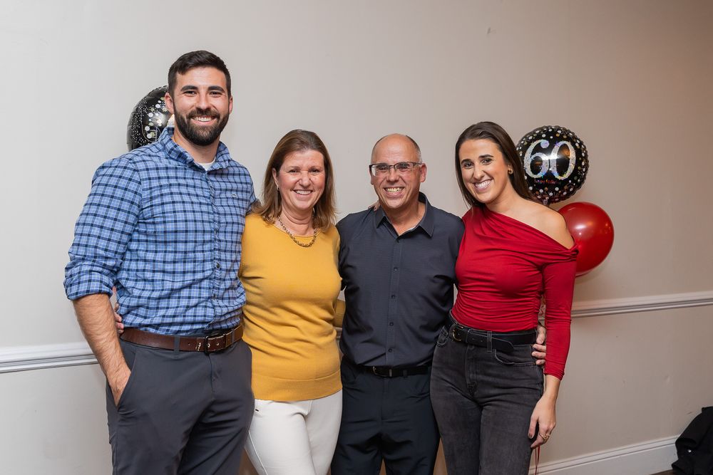 Group photo of party guests posing together with a 60th birthday decoration and red balloon visible.