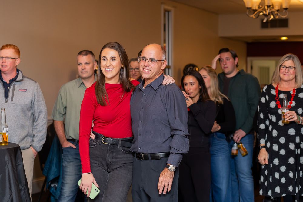 A group of guests gathered at an indoor celebration event with warm lighting and chandelier overhead.