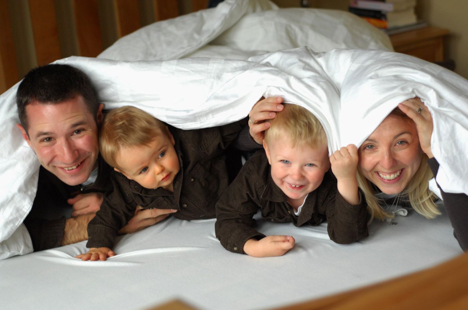 A playful family moment under white bedsheets capturing joy and laughter.
