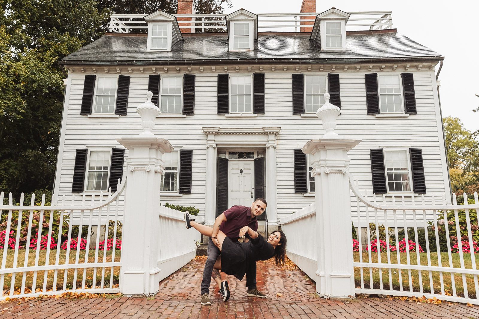 Fun portrait of couple being playful in front of historic white colonial building.